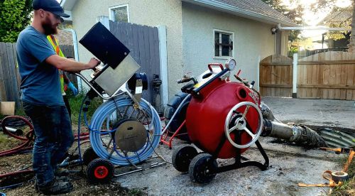 Trenchless pipe bursting equipment pushing new pipe through a small access pit in a Red Deer yard